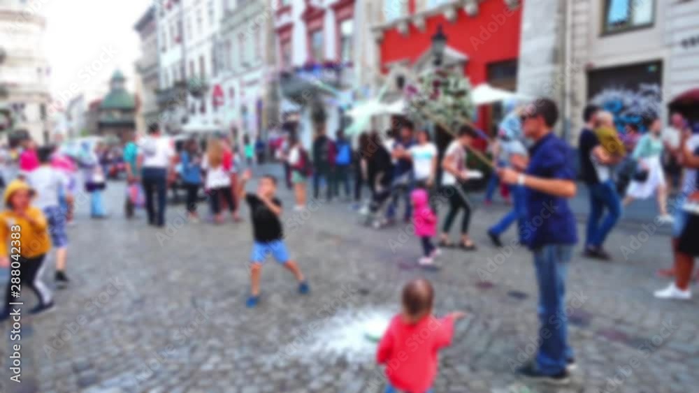 The man entertains children with soap bubbles in the city square. Out of focus. The man entertains children with soap bubbles in the city square. Out of focus.