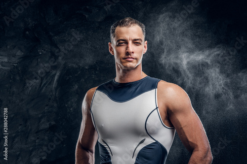 Portrait of muscular handsome man in wetsuit and with cloud of talc around over dark background. © Fxquadro