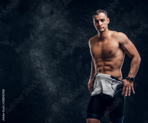 Hot sexy fit man is taking off his wetsuit in dark photo studio.