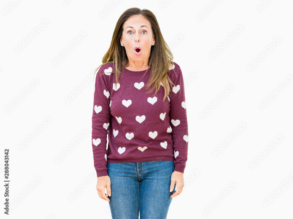 Beautiful middle age woman wearing hearts sweater over isolated background afraid and shocked with surprise expression, fear and excited face. Beautiful middle age woman wearing hearts sweater over isolated background afraid and shocked with surprise expression, fear and excited face.