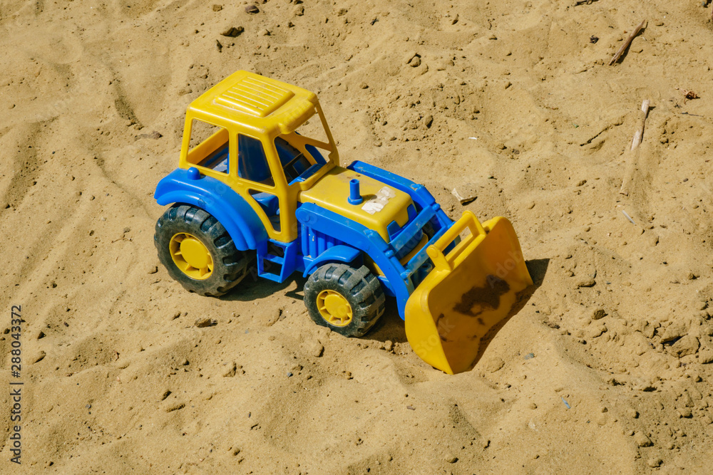 blue and yellow tractor on the sand. Baby's toys outdoor blue and yellow tractor on the sand. Baby's toys outdoor
