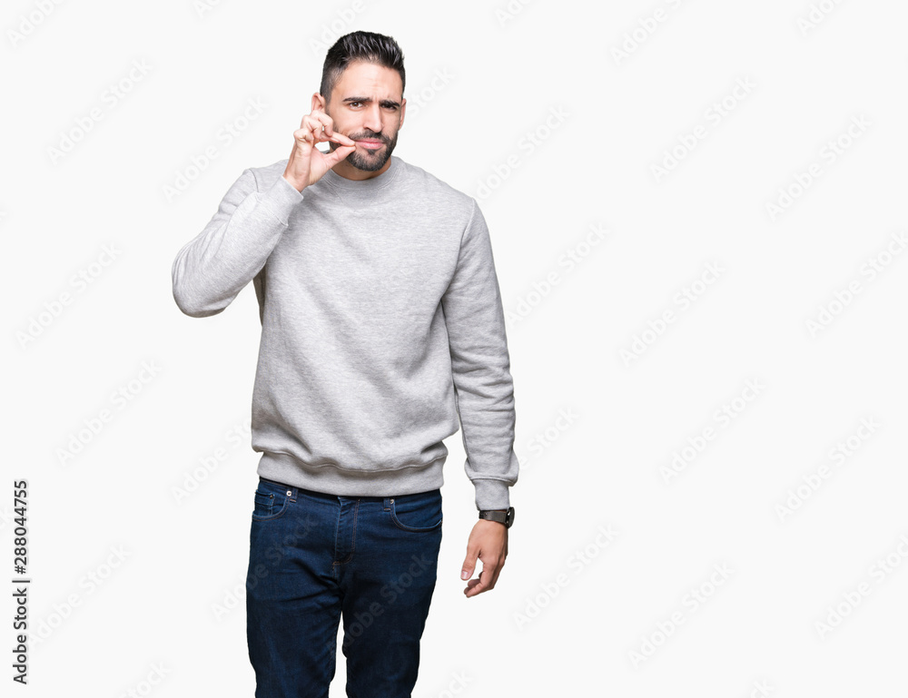 Young handsome man wearing sweatshirt over isolated background mouth and lips shut as zip with fingers. Secret and silent, taboo talking Young handsome man wearing sweatshirt over isolated background mouth and lips shut as zip with fingers. Secret and silent, taboo talking