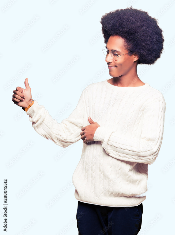 Young african american man with afro hair wearing glasses Looking proud, smiling doing thumbs up gesture to the side Young african american man with afro hair wearing glasses Looking proud, smiling doing thumbs up gesture to the side
