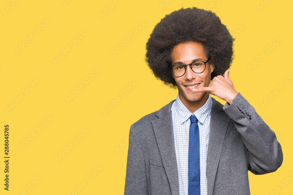 Young african american business man with afro hair wearing glasses smiling doing phone gesture with hand and fingers like talking on the telephone. Communicating concepts. Young african american business man with afro hair wearing glasses smiling doing phone gesture with hand and fingers like talking on the telephone. Communicating concepts.