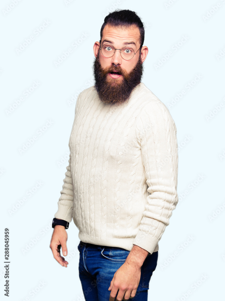 Young hipster man wearing glasses and winter sweater afraid and shocked with surprise expression, fear and excited face. Young hipster man wearing glasses and winter sweater afraid and shocked with surprise expression, fear and excited face.