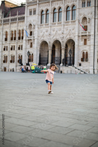 little girl child in shorts and a t-shirt stands near the Hungarian Parliament in Budapest 1