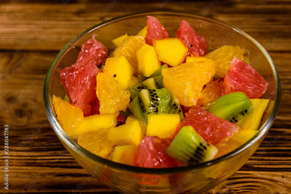 Salad with mango, oranges, grapefruit and kiwi fruits in a glass bowl on wooden table Salad with mango, oranges, grapefruit and kiwi fruits in a glass bowl on wooden table