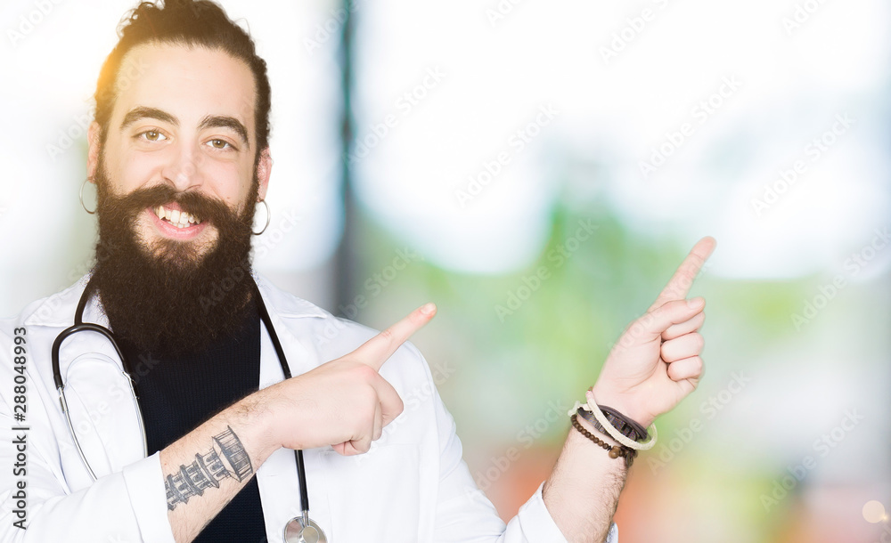Naklejka premium Doctor with long hair wearing medical coat and stethoscope smiling and looking at the camera pointing with two hands and fingers to the side.