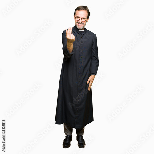 Middle age priest man wearing catholic robe Beckoning come here gesture with hand inviting happy and smiling