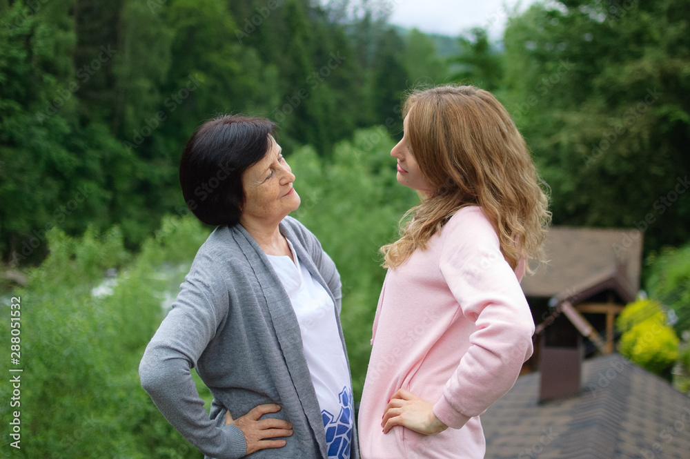 Outdoors portrait of happy mother and daughter looking to each other spending time together outside over landscape of forest and mountains. Outdoors portrait of happy mother and daughter looking to each other spending time together outside over landscape of forest and mountains.