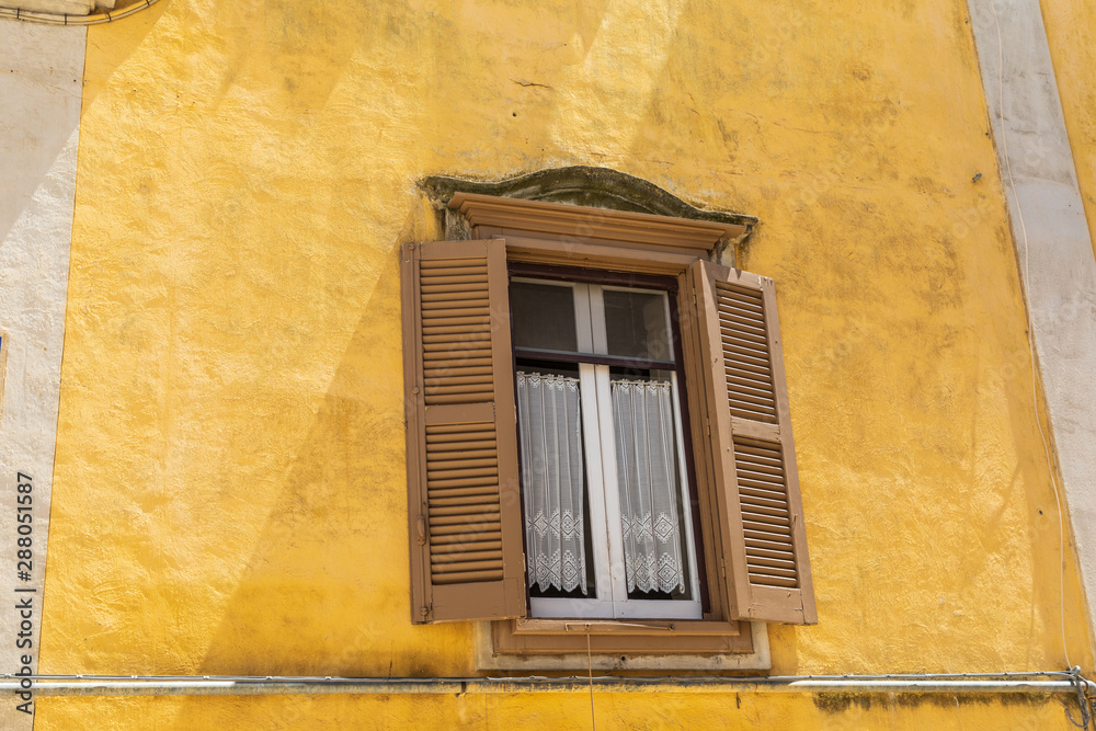 Italy, Basilicata, Province of Matera, Matera. Window with lace curtains and shutters in a yellow wall.