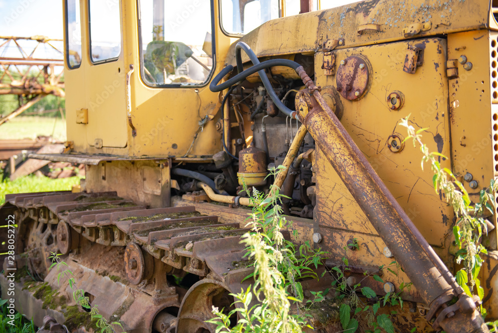 Abandoned farm equipment. The bulldozer covered with moss. Overgrown weeds tractor. Bulldozer is worth many, many years.