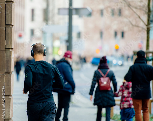 Rear view of unrecognizable people in city - man running with headphones and pedestrians discovering modern city