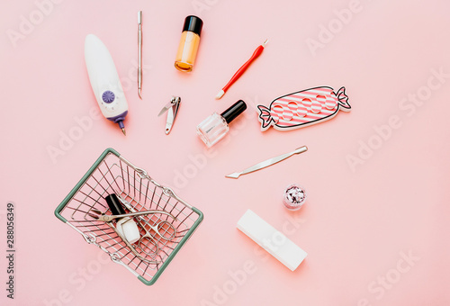 Manicure concept set on pink background. Nails tools, polishing nail buff, cuticle pusher, cuticle trimmer, nail file, scissors,toes separator,clippers, toenail clippers, gel polish in shopping basket