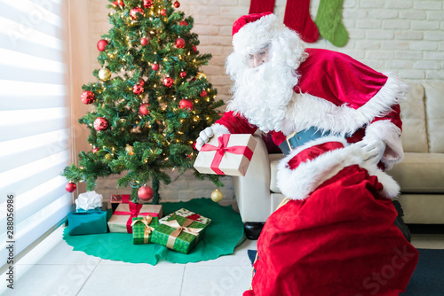 Santa Claus keeping Christmas gifts under tree at home © AntonioDiaz