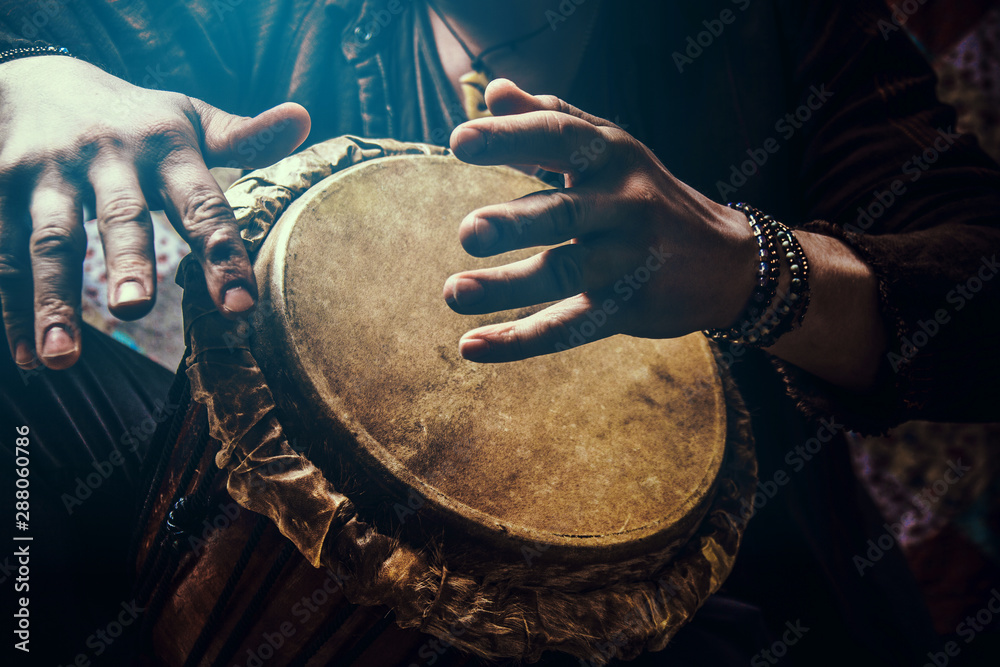 Fototapeta A man playing an ethnic percussion musical instrument jembe. Drummer playing african music