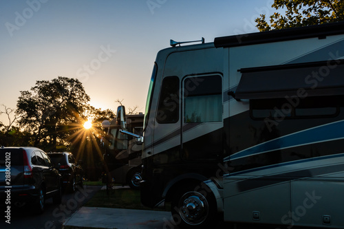 Rv parked at the park at golden hr with sunrise shining through the trees