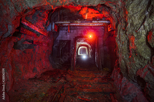 Dark dirty abandoned uranium mine with rusty remnants of railway color illuminated