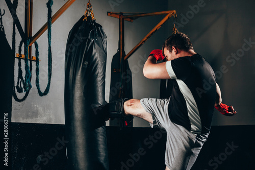 Canvas Print Muscular kickbox fighter exercising with punch bag at the gym