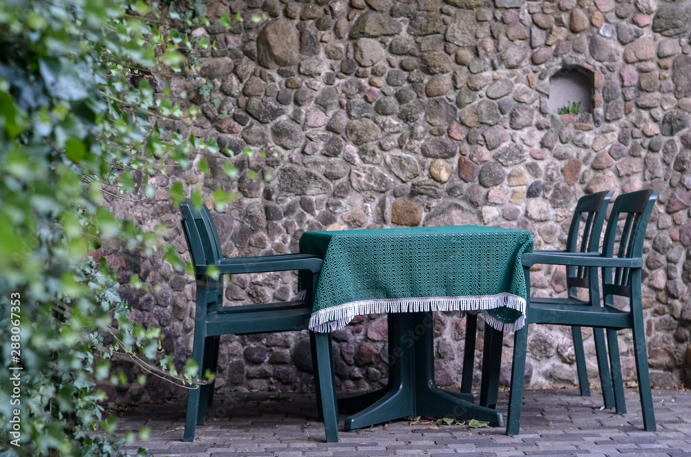 Green table and chairs on the background of stone wall in cozy outdoor terrace Green table and chairs on the background of stone wall in cozy outdoor terrace