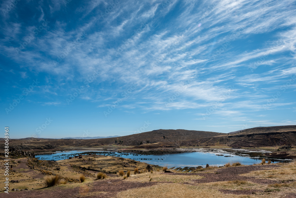 The thin whips strands of the Cirrus clouds create a beautiful contrasting backdrop to the dry, brown grass surrounding the wetlands of Sillustani in Peru