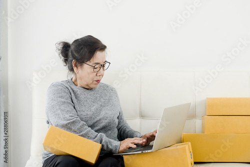 Asian senior woman using laptop while selling online with packaging, work at home concept. © nuiiko