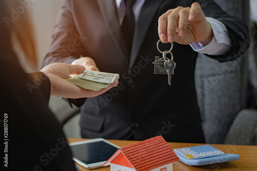 Agents are giving house keys of customer and holding dollar us bank at agency office. Agreement concept.