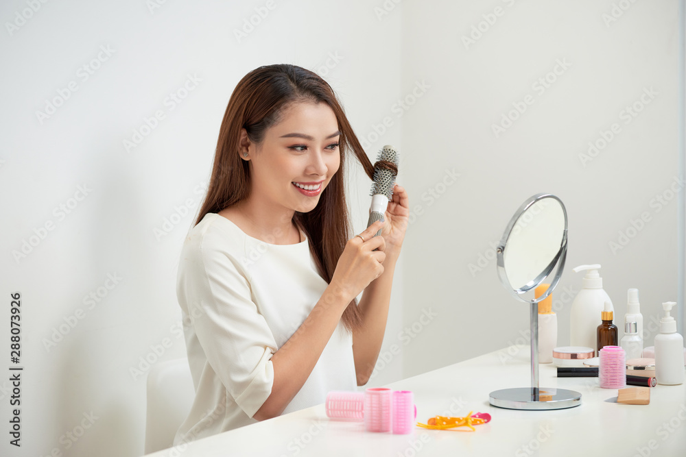 Getting rid of tangles. Beautiful young woman looking at her reflection in mirrorand brushing her long hair while sitting at the dressing table Getting rid of tangles. Beautiful young woman looking at her reflection in mirrorand brushing her long hair while sitting at the dressing table