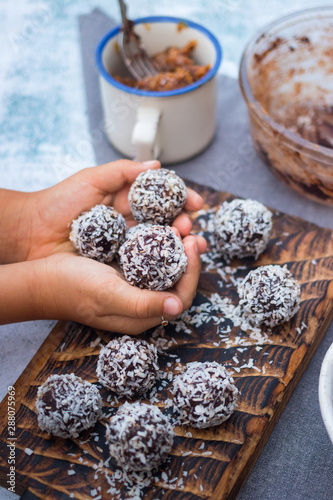 Little girl hands holds coconut sweet balls. Energy protein dessert with dates, cocoa, peanut butter.