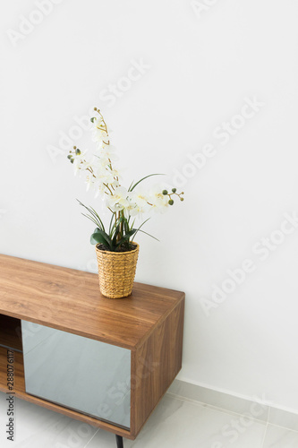 Fragment of living room interior wooden media stand potted orchid flower on white wall tiled floor background. Scandinavian minimalist style