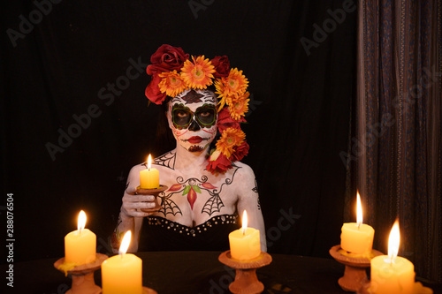 Woman bodypaint in day of the death ghoast decorate with flowers holding candle light in dark background photo