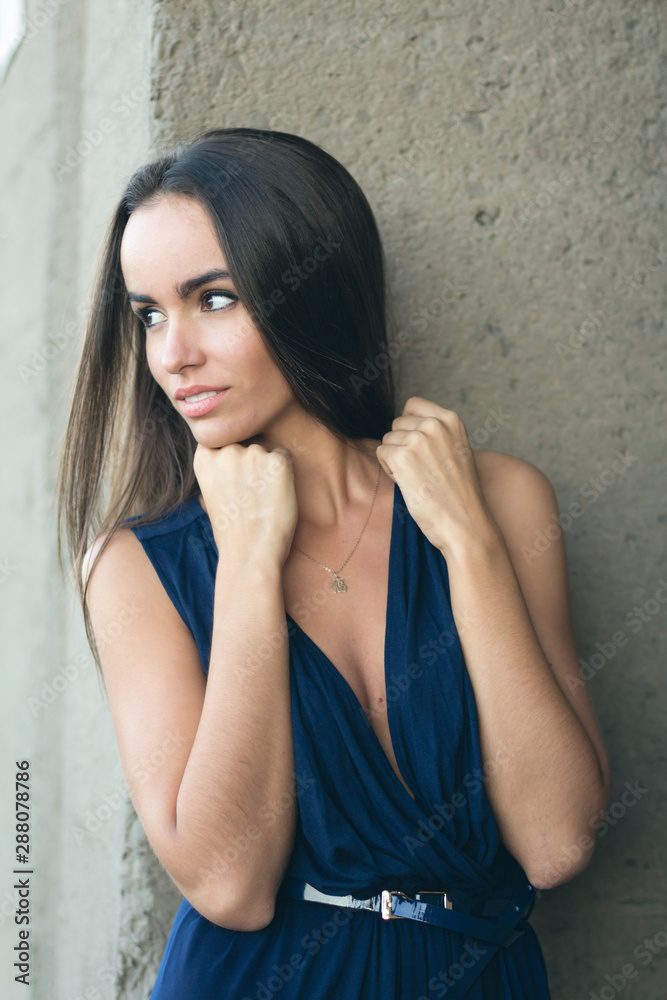 Fototapeta premium portrait of a fashionable woman in a blue dress with a neckline. Industrial wall in the background