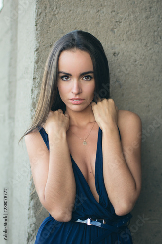 portrait of a fashionable woman in a blue dress with a neckline. Industrial wall in the background