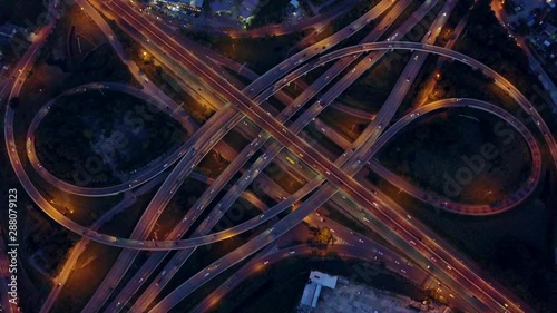 4K. Aerial view of road interchange or highway intersection with busy urban traffic speeding on the road at night. Junction network of transportation taken by drone.