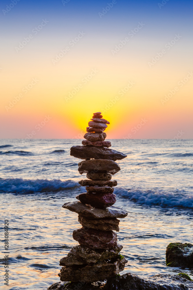 Obraz premium Zen Balancing Pebbles. Stack of pebbles on beach with sunrise on background
