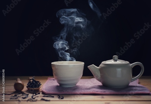 a cup of hot tea with tea pot , hot smoke, dark background.