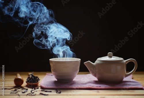 a cup of hot tea with tea pot , hot smoke, dark background.