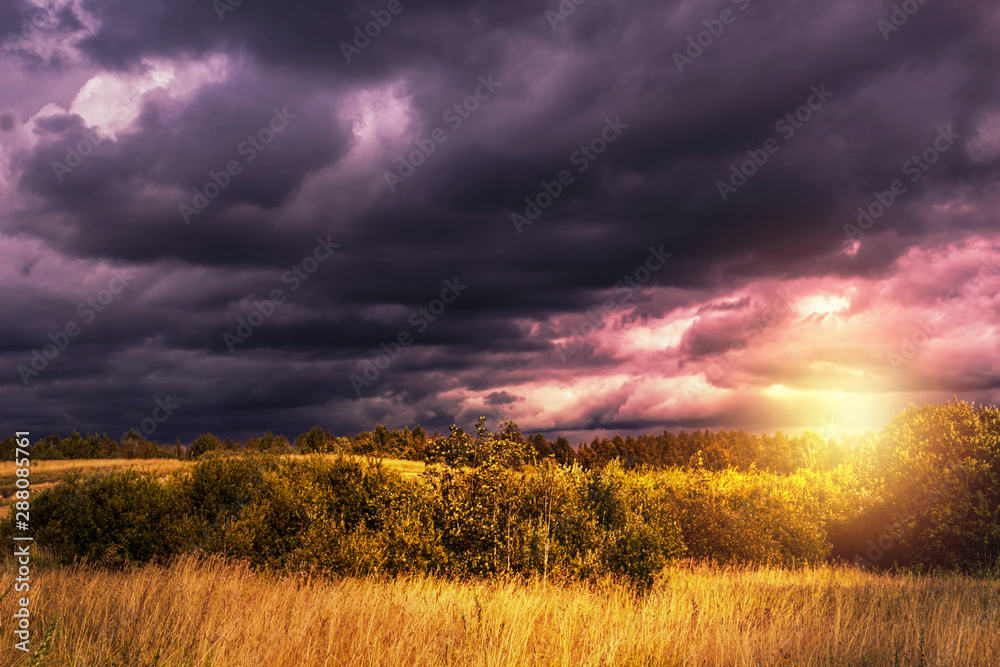 Dramatic Landscape with dark blue rainclouds before the thunderstorm in the field in summer time. Sunset with lens flare. Dramatic Landscape with dark blue rainclouds before the thunderstorm in the field in summer time. Sunset with lens flare.
