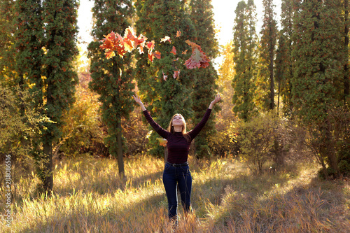 Happy woman throws autumn leaves in the park. Happy young teen girl in autumn scenery throwing leaves.