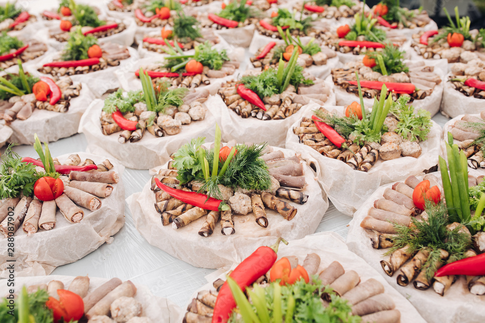 Beautiful creative composition of round platters served with delicious meat and vegetable rolls and decorated with fresh greenery and vegetables like tomatoes and cucumber. Banquet wedding reception