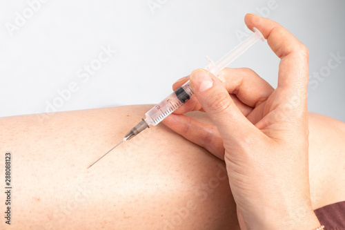 An extreme close up view of a young woman piercing the skin on her leg with a syringe needle filled with clear liquid. Heroin use and medicine concept photo