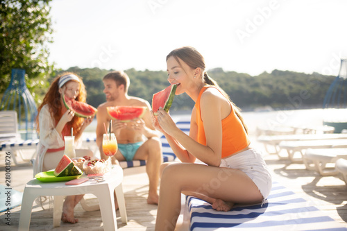 Slim woman wearing orange shirt eating watermelon