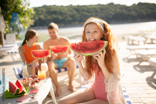 Red-haired woman making funny face while biting watermelon