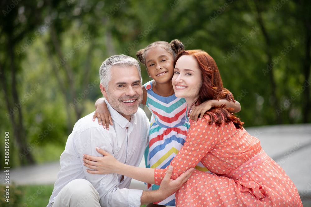 Loving foster parents hugging their lovely dark-skinned girl Loving foster parents hugging their lovely dark-skinned girl