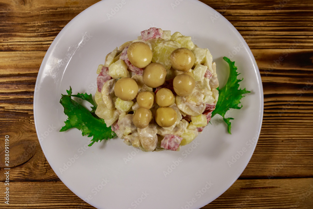 Potato salad with marinated mushrooms, sausage, onion and mayonnaise on wooden table