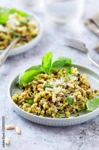 Fregola sarda with pesto sauce garnished with fresh basil, parmesan cheese and pine nuts