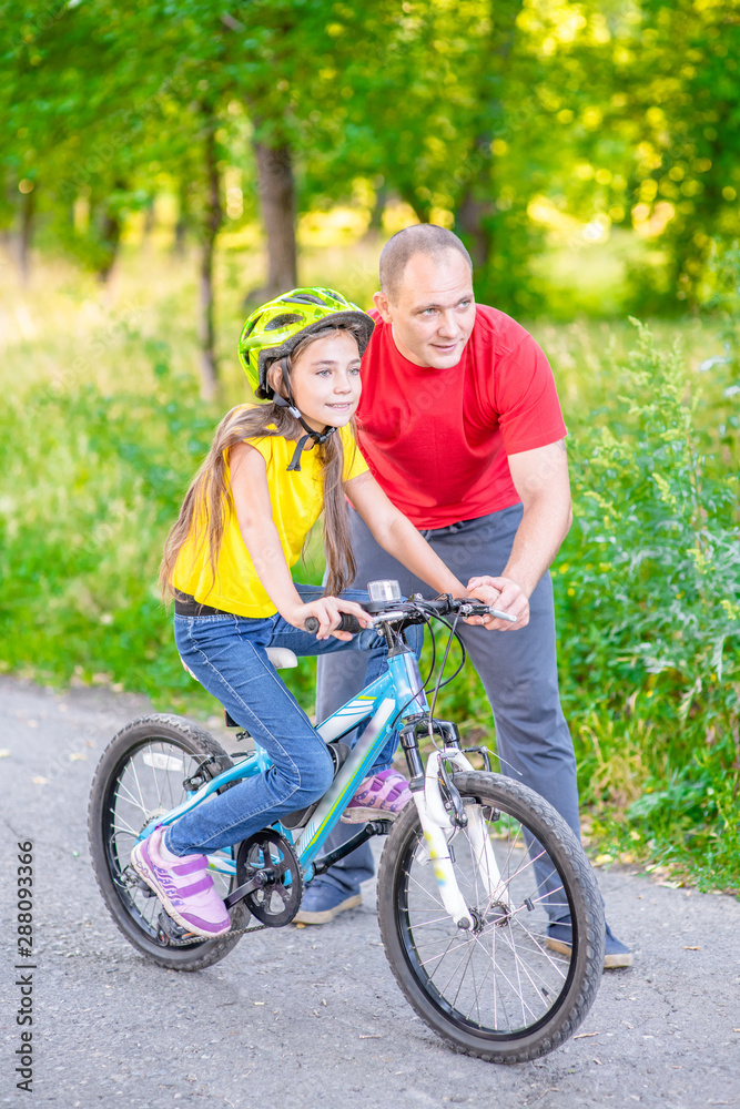 Happy family. Father teaches his daughter to ride a bicycle in the summer park