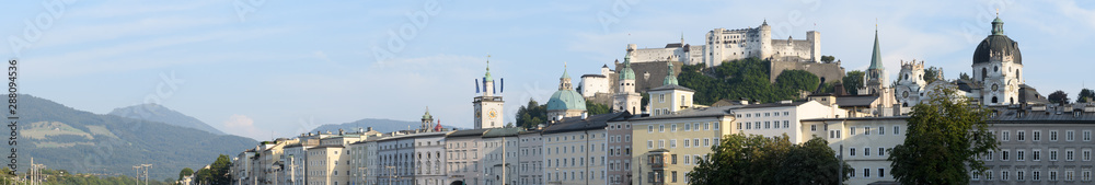 Panorama of houses along the embankment of the Salzach river, mountains and with the Hohensalzburg fortress in Salzburg, Austria.