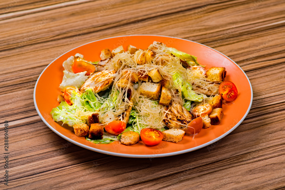 Caesar salad with chicken and leaves of salana on an orange plate on a wooden table Caesar salad with chicken and leaves of salana on an orange plate on a wooden table