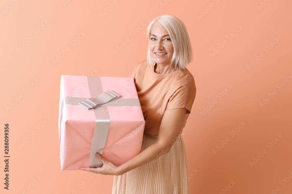 Mature woman with gift box on color background Mature woman with gift box on color background